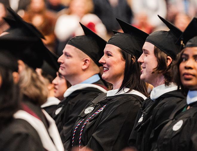 students standing while wearing regalia during snu commencement ceremonies